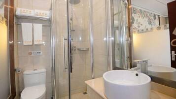 Een moderne badkamer met een douchecabine van glas, een wit toilet en een rond wastafeltje met een spiegel erboven.