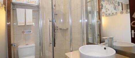 A modern bathroom with a glass-enclosed shower, a white toilet, and a round sink with a mirror above it.
