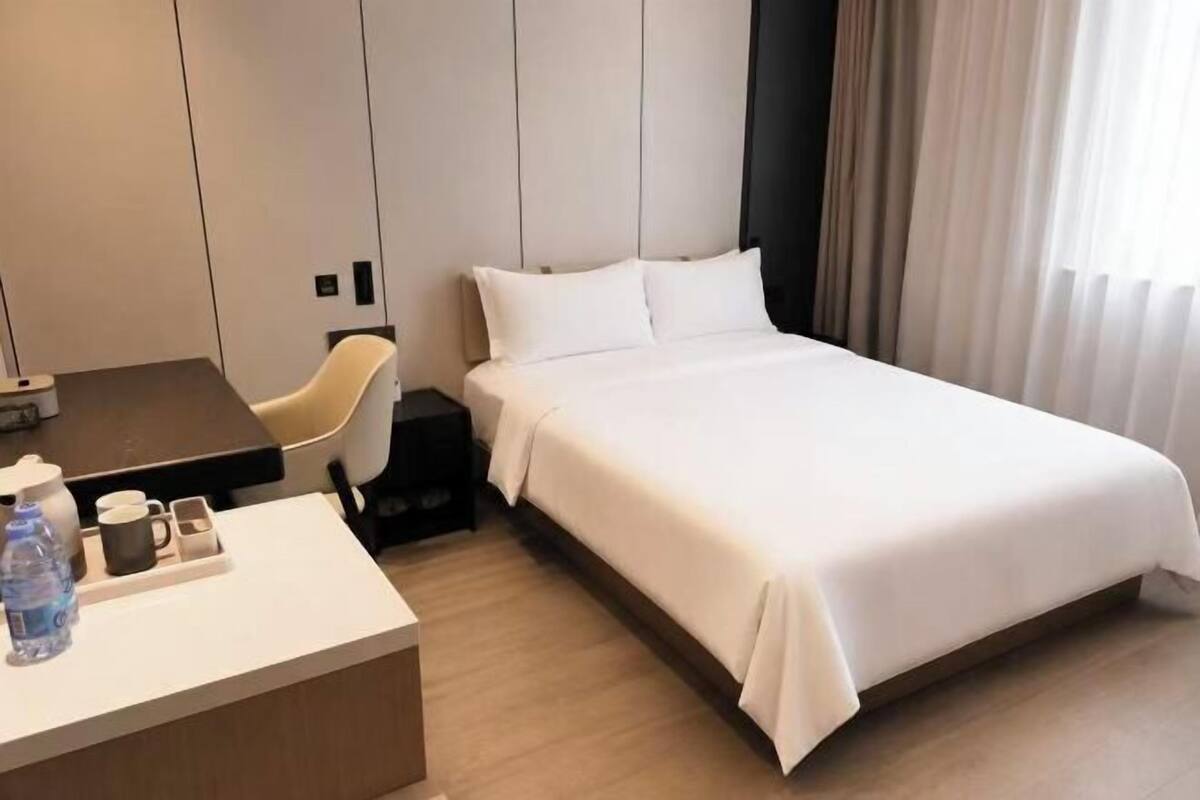 Ein Hotelzimmer mit einem Bett, einem Schreibtisch mit Stuhl, einer Kaffeemaschine und einer Wasserflasche.