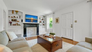A living room with a fireplace, a sofa, a coffee table, and a bookshelf. - Charming 3/2 Midtown Home. Minutes from FSU. Fenced Backyard. Pet-Friendly. (Tallahassee)
