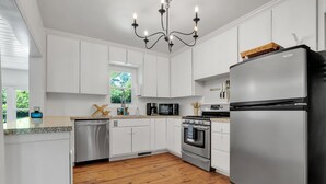 A modern kitchen with white cabinets, stainless steel appliances, and a wooden floor. - Charming 3/2 Midtown Home. Minutes from FSU. Fenced Backyard. Pet-Friendly. (Tallahassee)