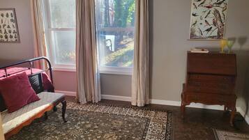 A room with a bed, a wooden dresser, a rug, a window with curtains, and a wall-mounted bird illustration.