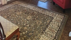 En stue med et stort gulvtæppe med mønster, en træstol, en rød sofa og en dør med glasmaleri.
