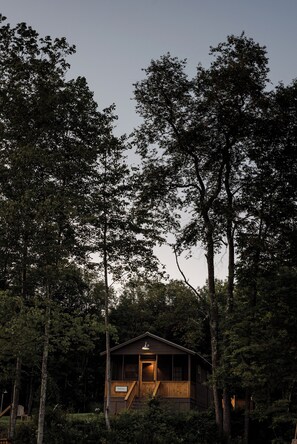 A cabin surrounded by tall trees at dusk.