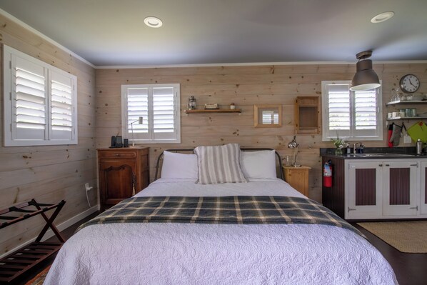 A cozy bedroom with a bed, bedside tables, a wooden wardrobe, and a small kitchenette.
