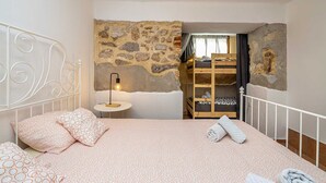 Un dormitorio con pared de piedra, cama con ropa de cama estampada, lámpara de noche y una cama litera de madera.