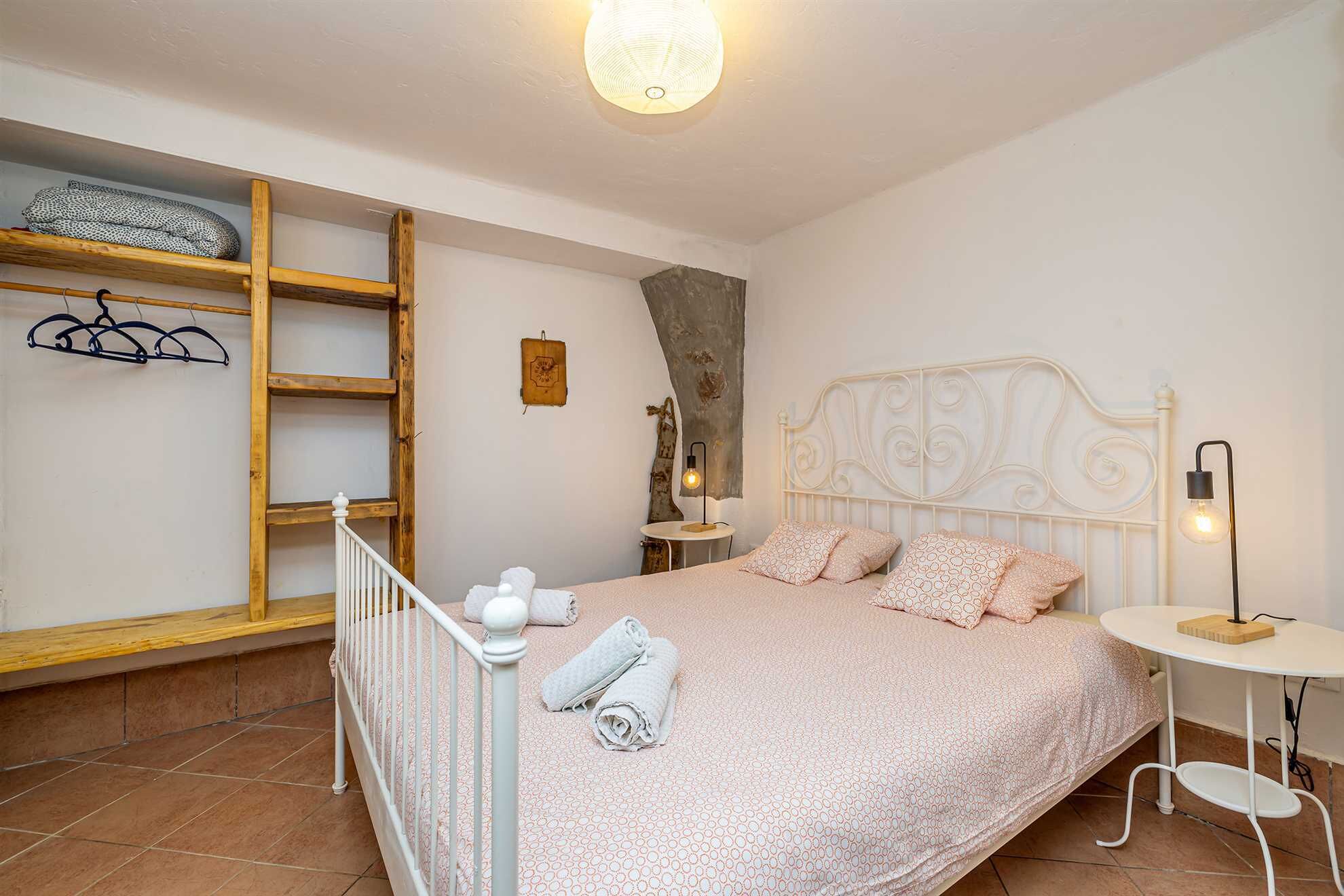 Un dormitorio con una cama, una estantería de madera, una mesita pequeña y una lámpara de pared.