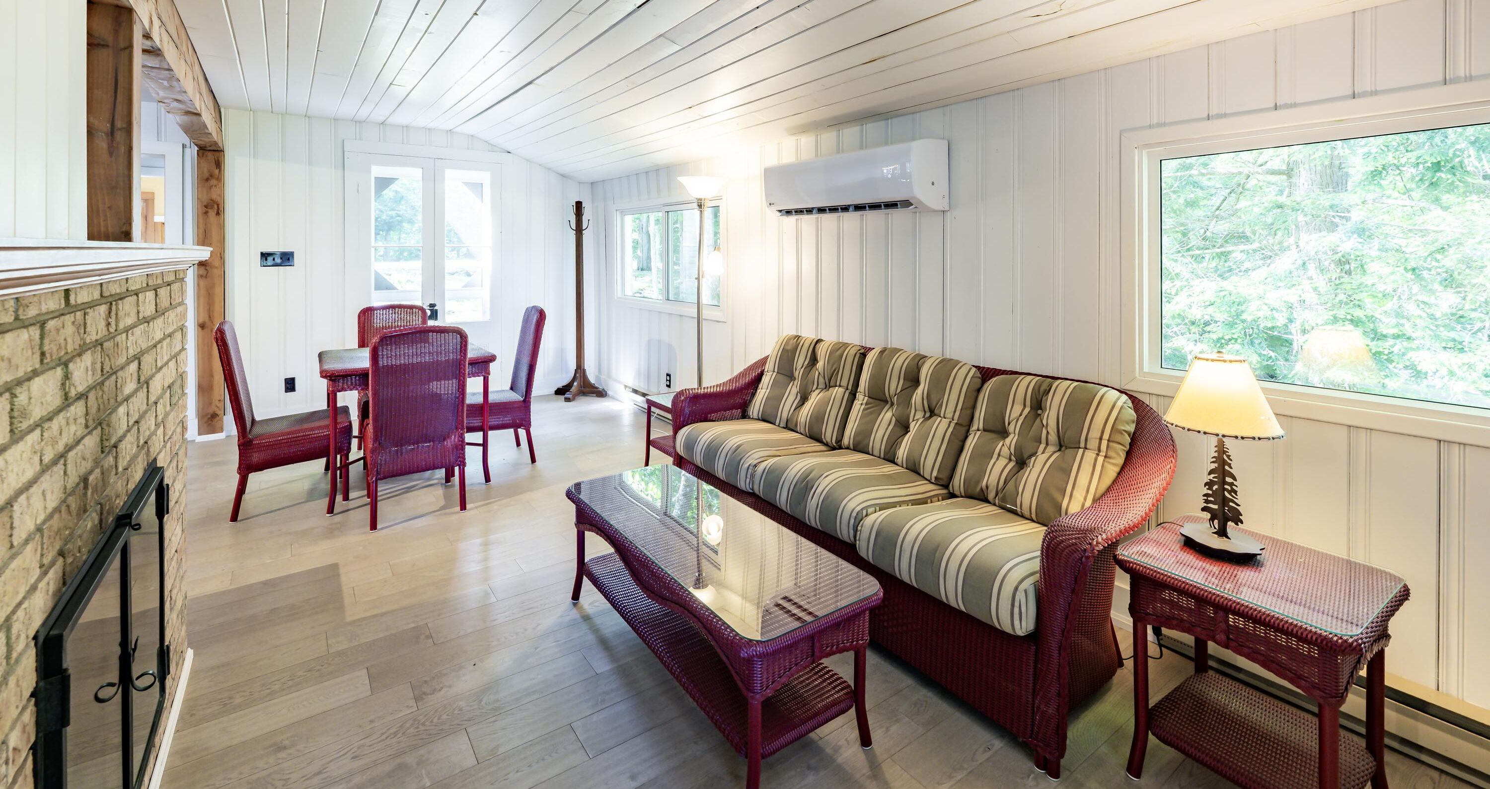 A cozy living room with a striped sofa, red wicker chairs, a glass-top coffee table, and a lamp.