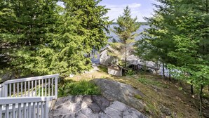 A cabin with a stone staircase leading up to a deck overlooking a lake, surrounded by dense forest.