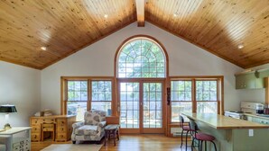 A spacious kitchen with a large window, wooden ceiling, and a view of the outdoors.