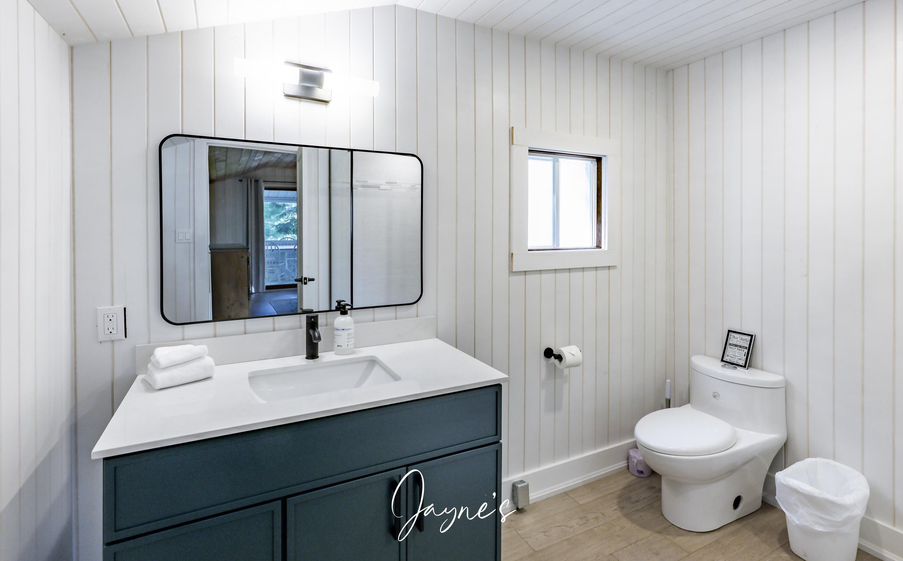 A bathroom with a white vanity, a large mirror, a toilet, and a window.