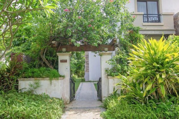 A gated entrance with a pathway leading to a building, surrounded by lush greenery and a pergola overhead. - Huizhou Shuangyuewan Junlai Victoria Villa (Huidong)