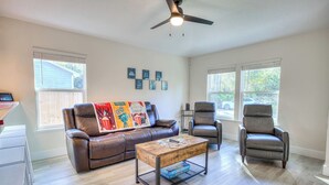 A living room with a brown leather couch, a coffee table, and two leather armchairs. There are framed pictures on the wall and a ceiling fan.