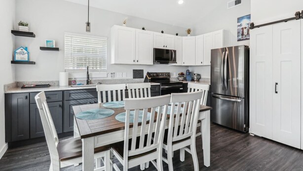 A modern kitchen with white cabinets, a stainless steel refrigerator, and a dining area with white chairs and a wooden table.