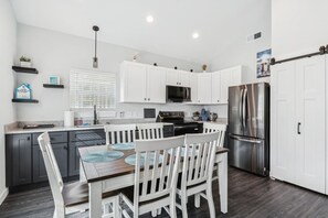 Een moderne keuken met witte kasten, een roestvrijstalen koelkast en een eethoek met witte stoelen en een houten tafel.