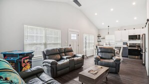 A spacious living area with a large leather sofa, a coffee table, and a gaming table.
