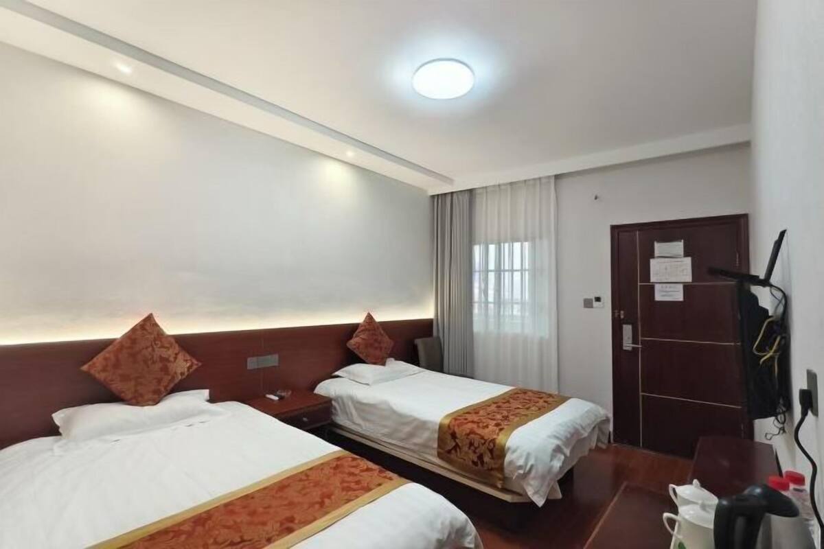 A hotel room with two beds, a desk, a chair, a wardrobe, and a window with curtains.
