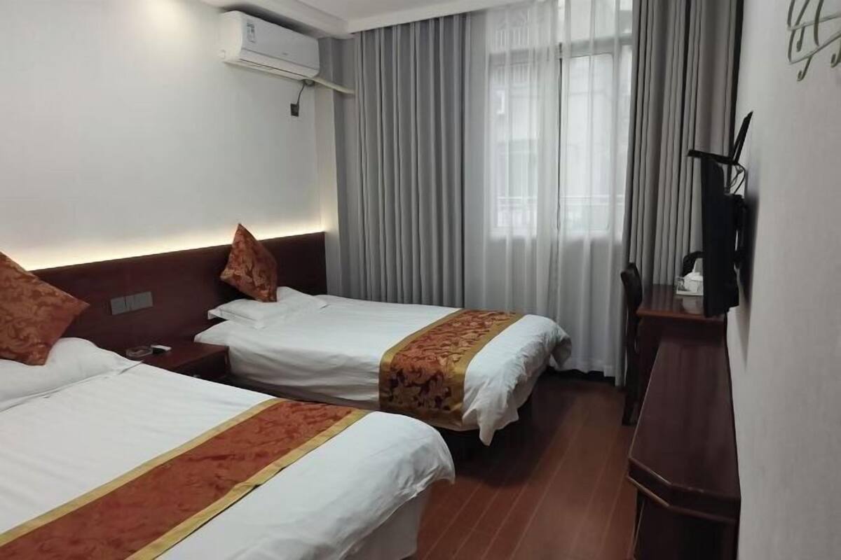 A hotel room with two beds, a wooden floor, a desk, and a window with curtains.