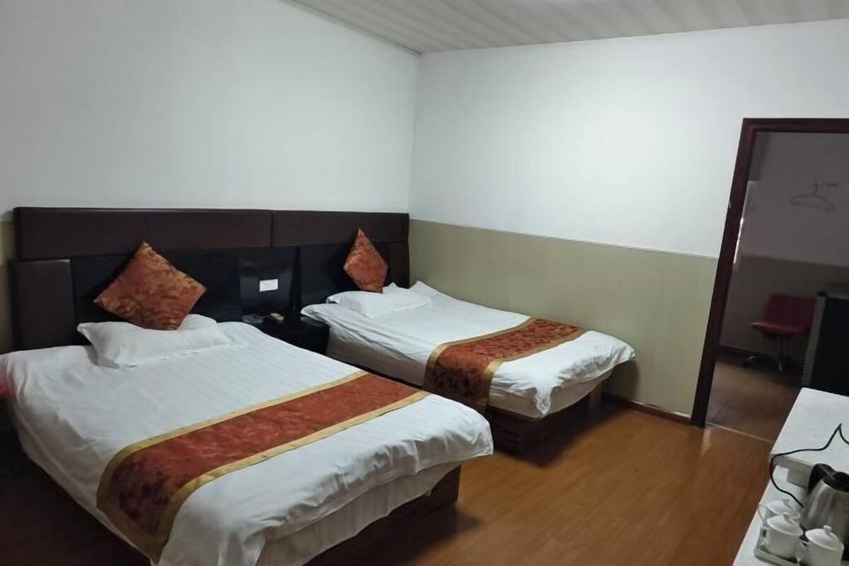 A hotel room with two beds, a wooden floor, and a desk with a chair.