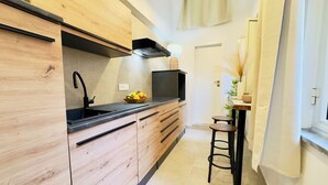 Une cuisine compacte dotée de meubles en bois, d’un plan de travail noir et d’un petit coin repas avec un tabouret.