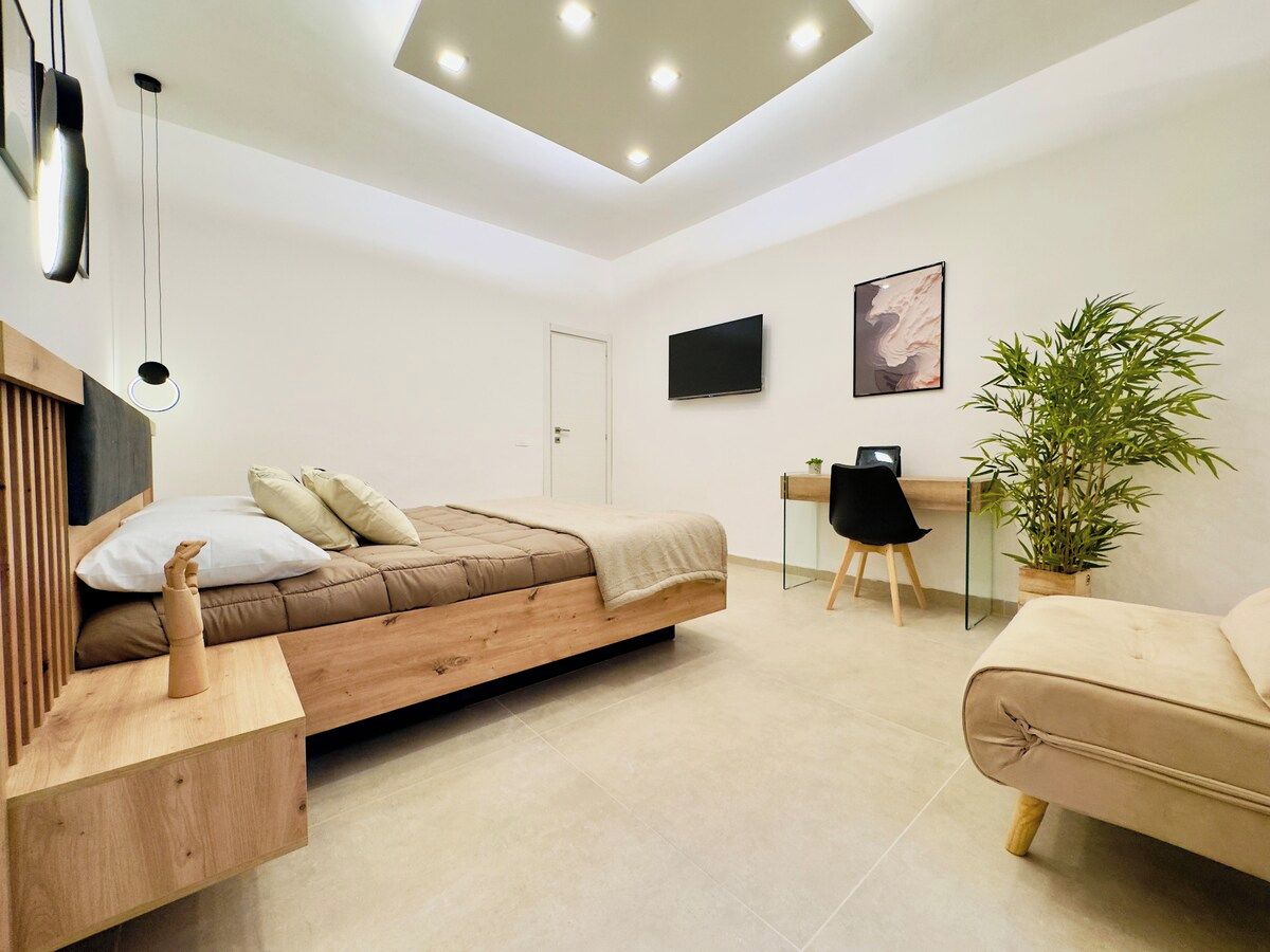 A modern bedroom with a bed, bedside table, chair, desk, and a potted plant.