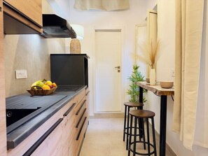 A kitchen with a black countertop, wooden cabinets, a fruit bowl, a stove, and a small stool.