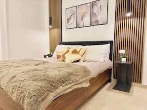 A modern bedroom with a wooden bed frame, a fluffy beige throw blanket, and a bedside table with a plant.