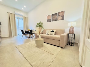 A living room with a sofa, a coffee table, a lamp, and a dining area with chairs and a table.