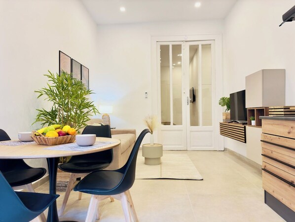 A modern living room with a dining area, featuring a round table with chairs, a sofa, and a large potted plant.
