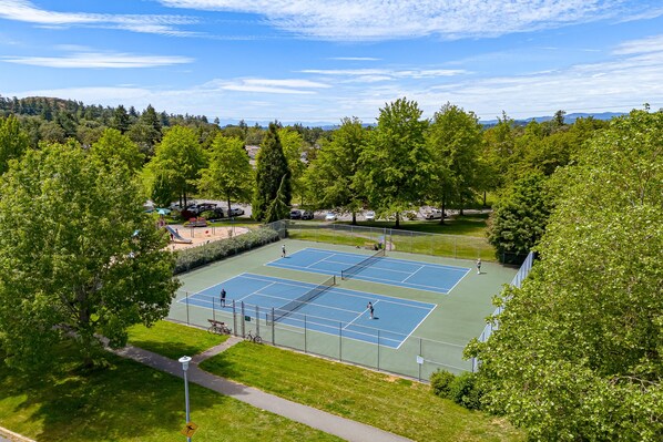 A tennis court surrounded by trees and a parking area.