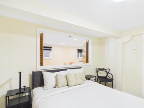 A hotel room with a bed, a nightstand, a chair, a small table, and a large mirror on the wall.