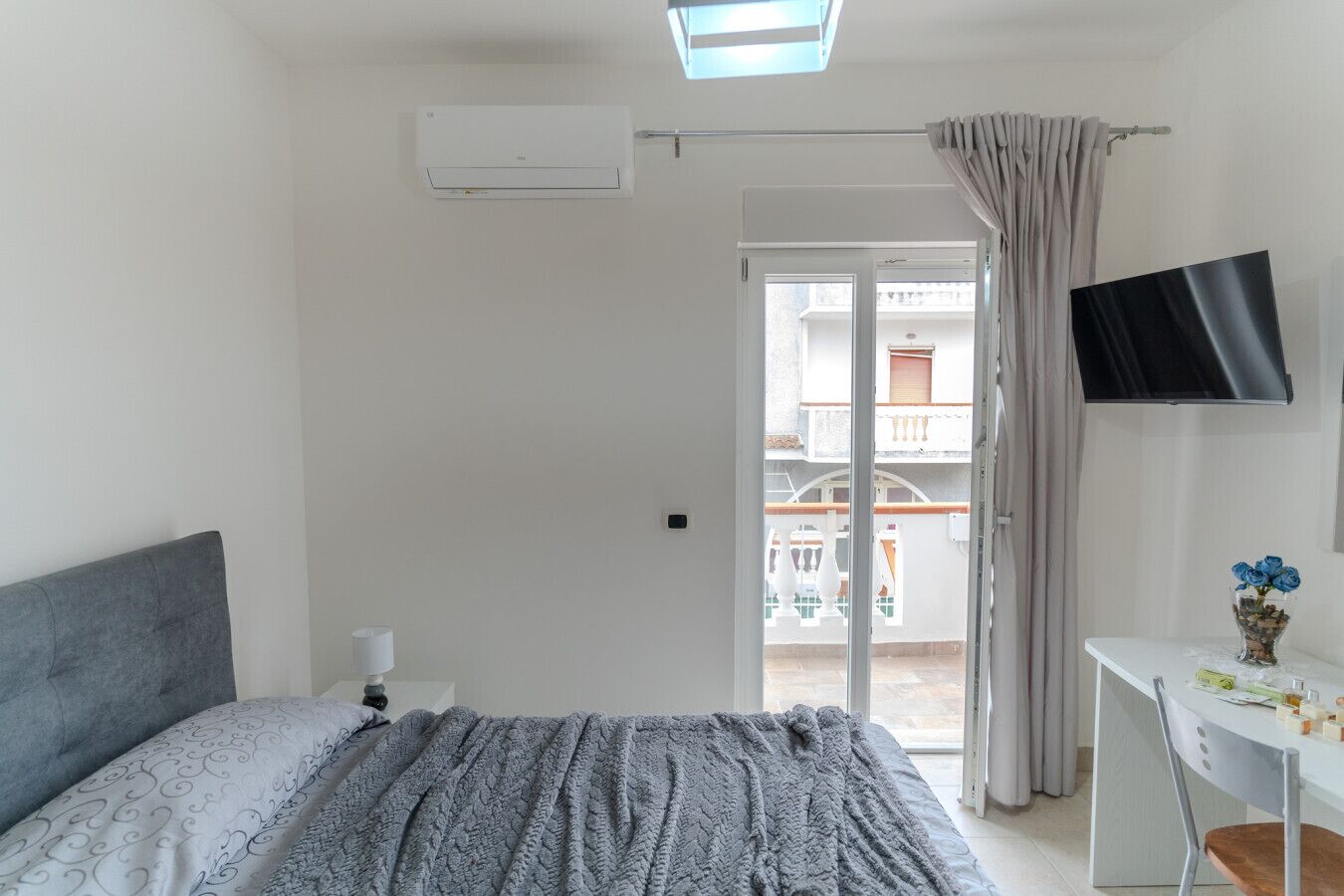 Una camera da letto con un letto, un comodino, una TV e un balcone con vista.