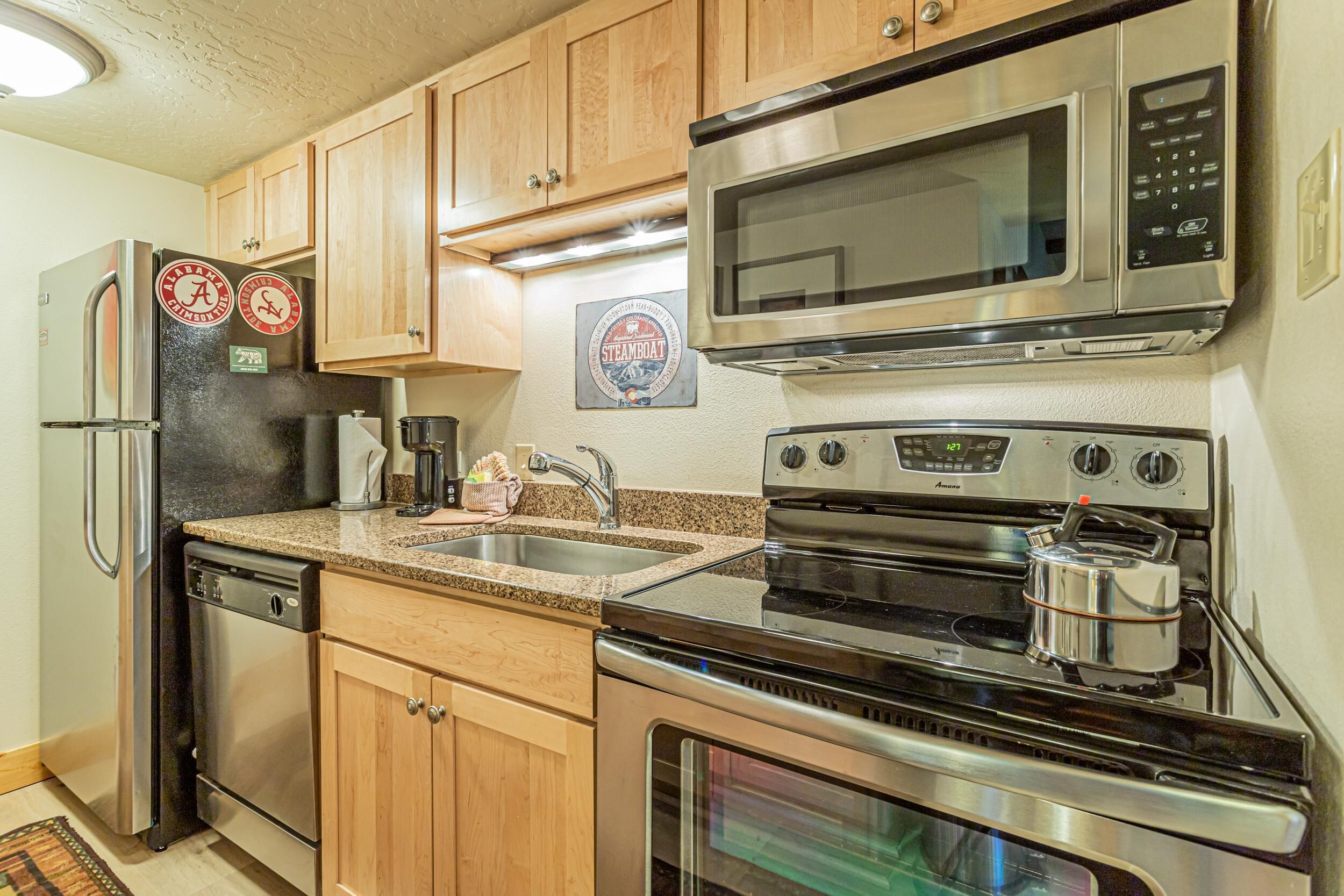 A modern kitchen with stainless steel appliances, wooden cabinets, and a granite countertop.