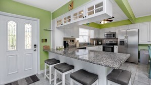 Une cuisine moderne dotée d’un îlot central, de tabourets de bar, d’appareils électroménagers en acier inoxydable et d’un mur d’accent vert.