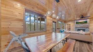 A wooden cabin interior with a dining table, benches, a stone fireplace, and large windows. - Spacious 5-bedroom cabin in marvelous Pigeon Forge with AC, WiFi (Pigeon Forge)