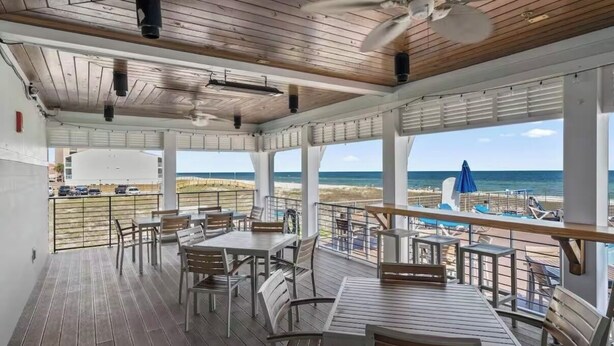 A covered outdoor dining area with tables and chairs, overlooking a beach.