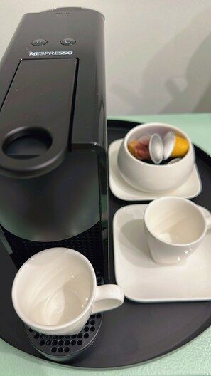 En Nespresso-kaffemaskine på et fad med to hvide kopper og en skål med en citron og en appelsinskive.