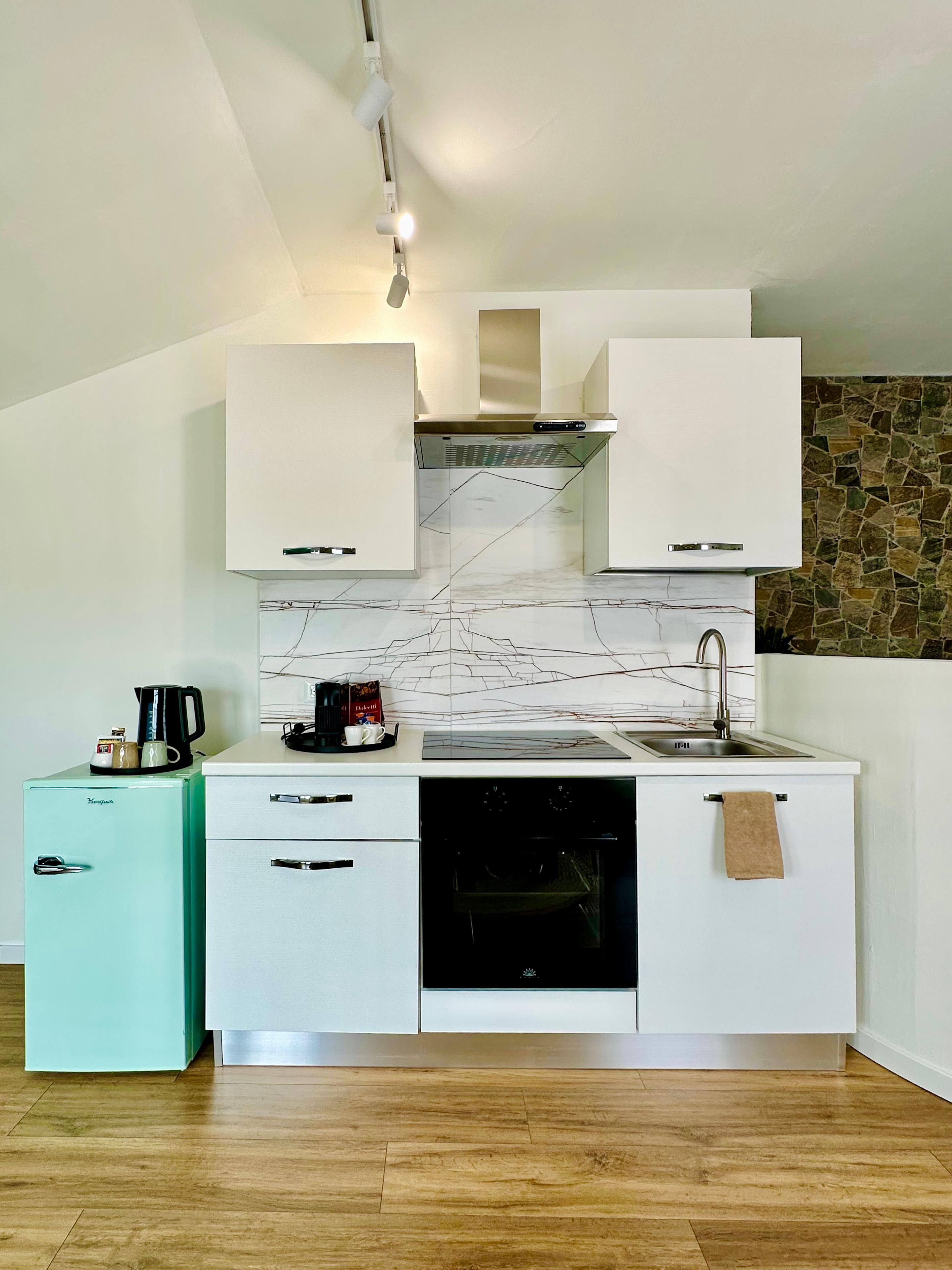 A compact kitchen with white cabinets, a marble backsplash, a built-in oven, and a small fridge.