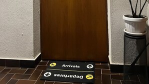 A hotel entrance with a wooden door, a sign above it, a potted plant, and a mat indicating arrivals and departures. - Catullo Loft (Dossobuono)