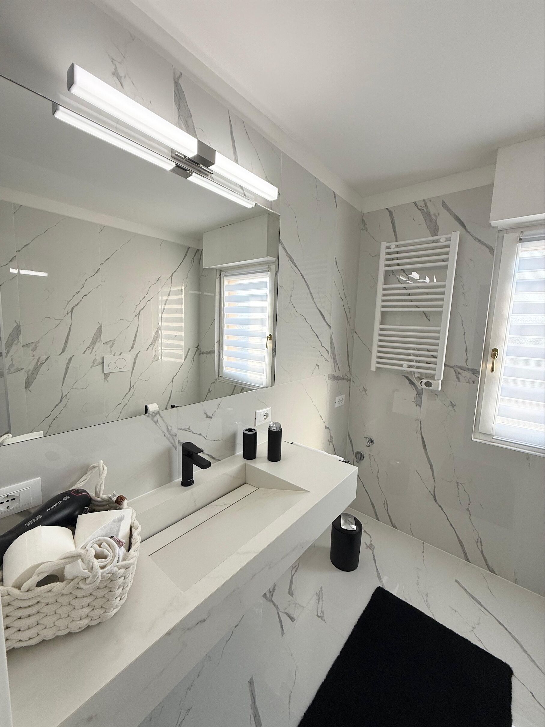A modern bathroom with a marble backsplash, a large mirror, a black towel, and a white sink.