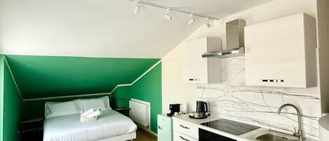 A compact room with a bed, kitchenette, and a dining area.