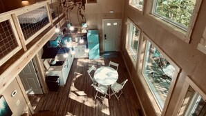 Une pièce spacieuse avec un plafond haut, de grandes fenêtres, un coin repas et une cuisine.
