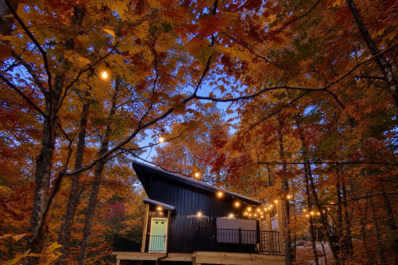 A cabin with a wooden deck and a lighted entrance, surrounded by autumn foliage.