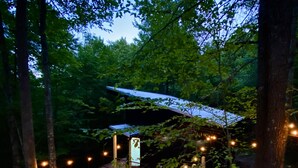 Une terrasse en bois avec un jacuzzi, entourée d’arbres et illuminée de guirlandes lumineuses.