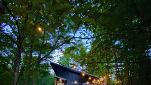 Une cabane en bois dotée d’un balcon, entourée d’arbres et illuminée de guirlandes lumineuses.