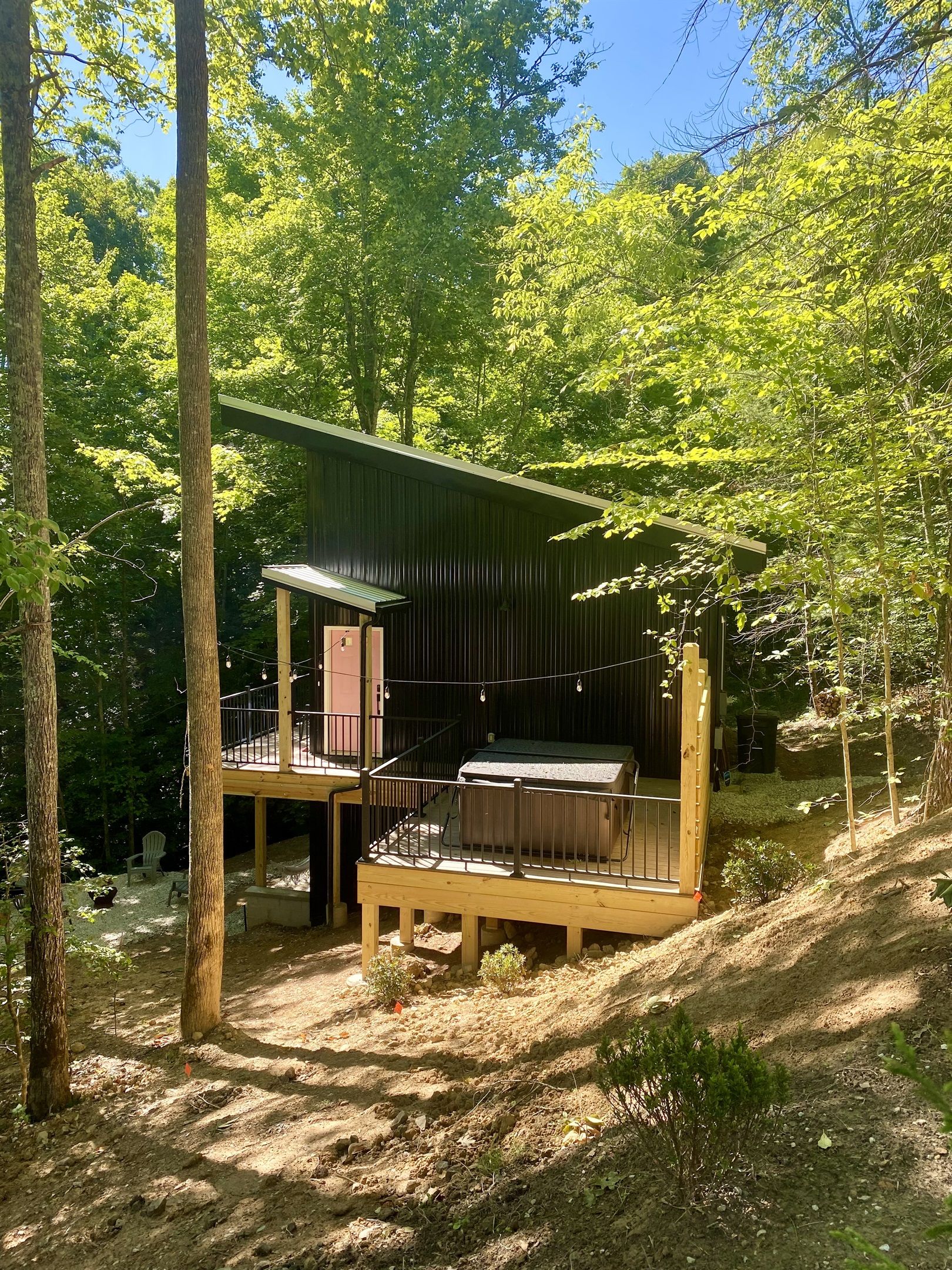 A rustic cabin with a wooden deck and a metal roof, surrounded by dense forest.