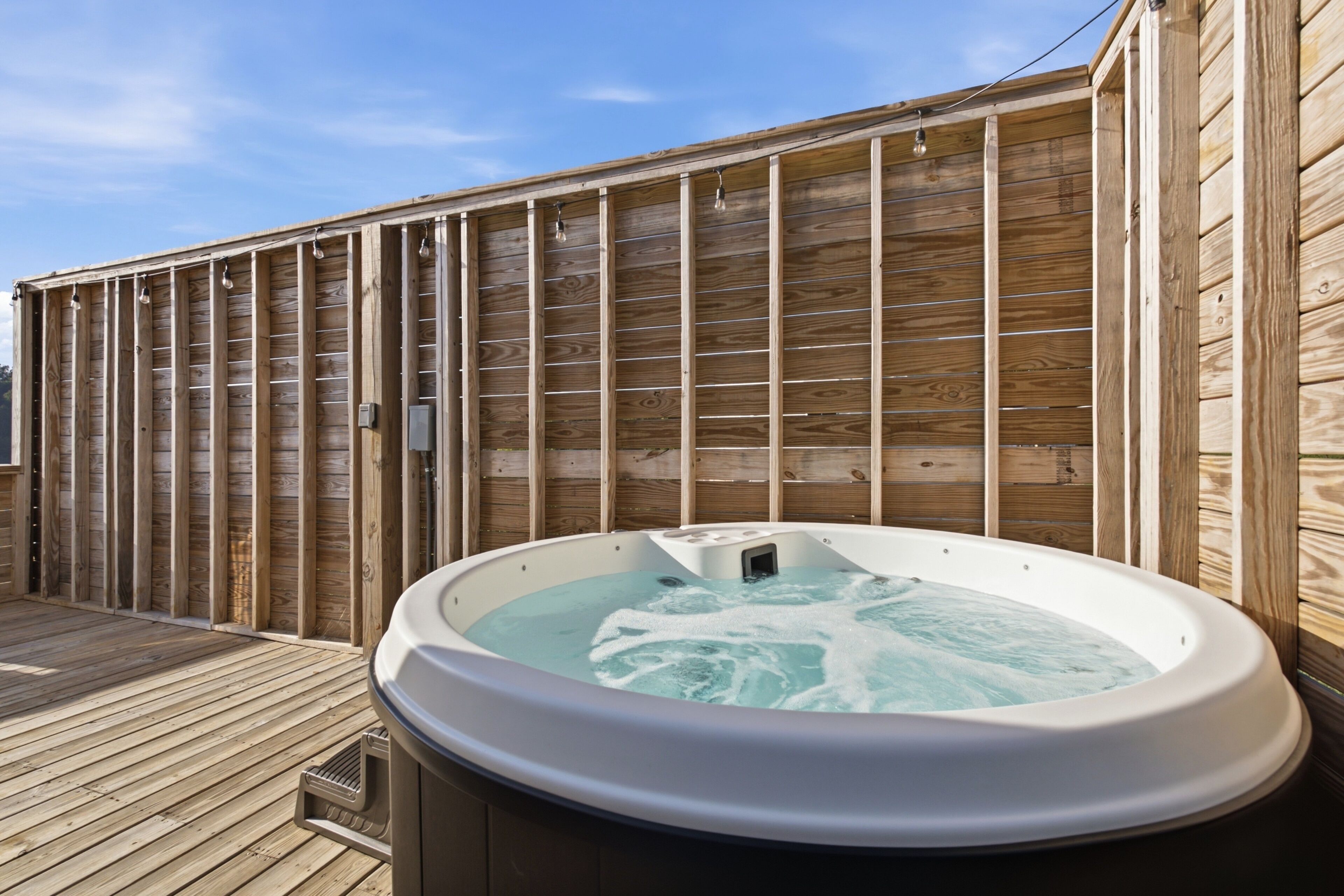 Un bain à remous sur une terrasse en bois, avec un mur en bois en arrière-plan.