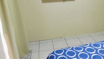 Une chambre avec un lit, un téléviseur fixé au mur et un rideau.