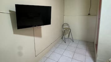 Una habitación con televisión de pantalla plana montada en la pared, una pequeña silla plegable y un equipo de aire acondicionado en el techo.