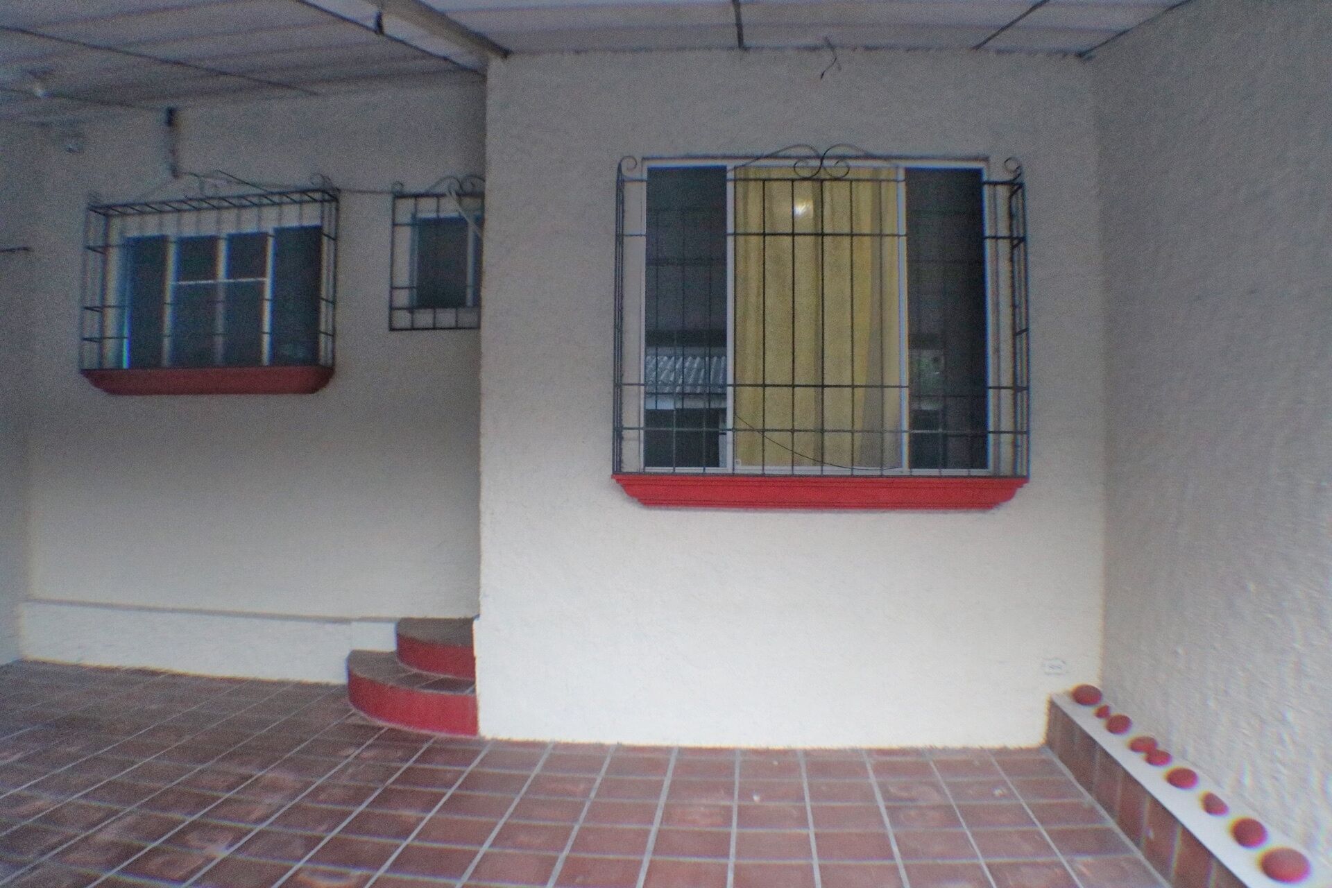 Una habitación con suelo de baldosas, una ventana con reja metálica y un repisa roja.